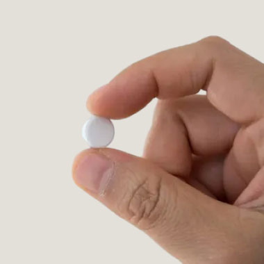 Nahaufnahme einer weißen Tablette zwischen Daumen und Zeigefinger