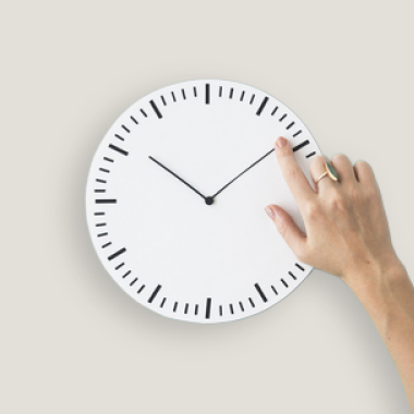Hand berührt das Zifferblatt einer analogen Uhr.