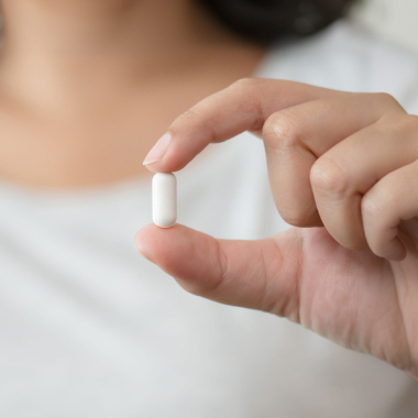 Nahaufnahme einer Frau, die eine weiße Tablette zwischen dem Daumen und Zeigefinger hält