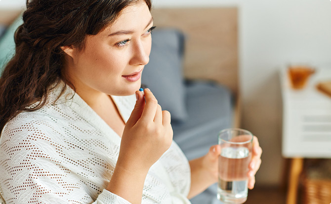 Junge übergewichtige Frau sitzt auf einem Bett und nimmt eine Kapsel mit Wasser ein