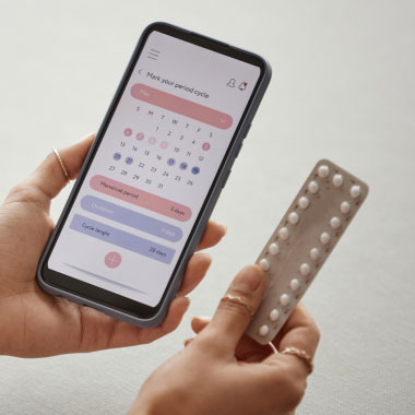 Nahaufnahme einer Frau, die ein Smartphone mit Kalender und Antibabypille hält