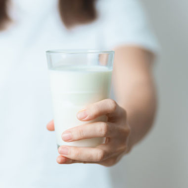 Nahaufnahme einer Frau, die ein Glas Milch und ein Medikament hält.