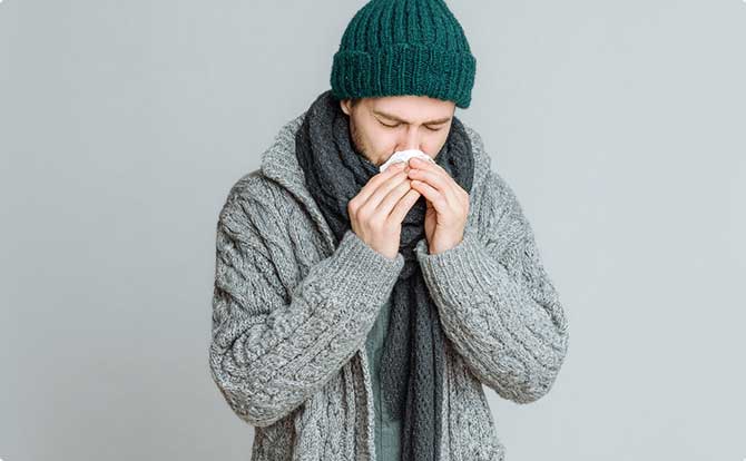 En ung mand foran en grøn baggrund med influenza, der pudser næse.