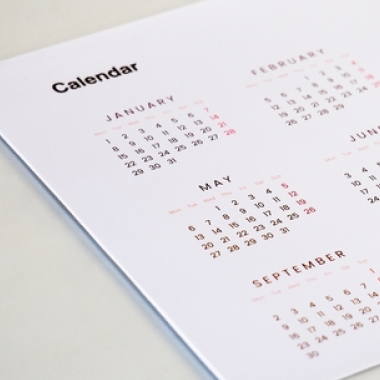 Close-up of a hand holding a pen and pointing at a date on a calendar