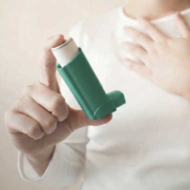 A young woman using a white and green inhaler