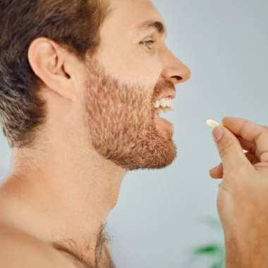 A side profile of a bearded man taking a white tablet