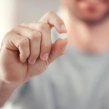 Close up of a man holding up a white pill