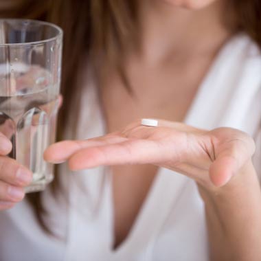 A woman taking a capsule with a glass of water