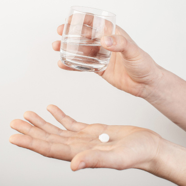 A person holding a glass of water in one hand and a white tablet in the other