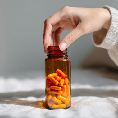 A hand is grabbing an unbranded bottle of pills.