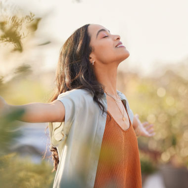 A young woman smiling with her arms outstretched in nature