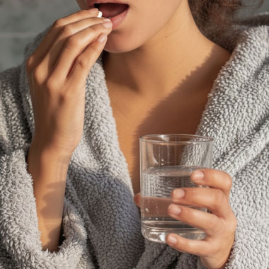 A woman taking a tablet with a glass of water