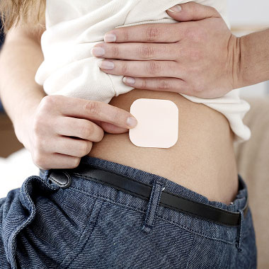 Une femme qui soulève légèrement son haut et applique un patch contraceptif sur son abdomen