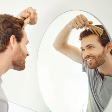 Un homme confiant souriant dans le miroir en se coiffant