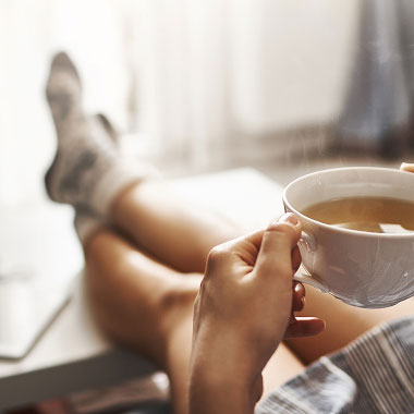 Femme avec une tasse de thé dans la main, les jambes allongées sur un bureau