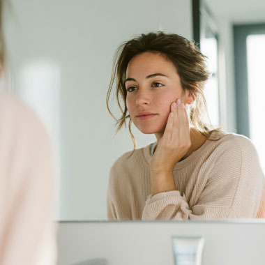 Jeune femme observant sa peau irritée dans le miroir.
