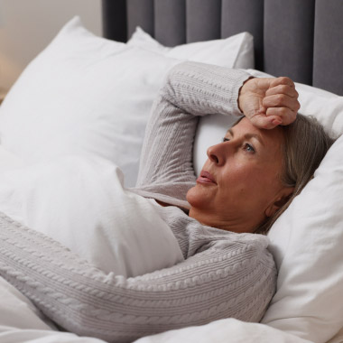 Une femme allongée éveillée dans son lit, une main posée sur le front