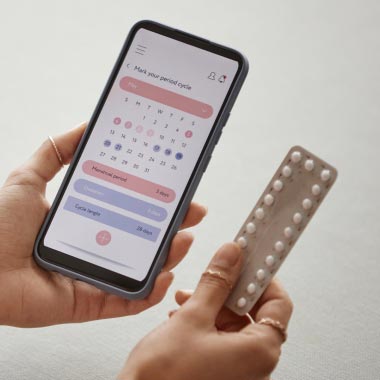 Gros plan sur la main d’une femme tenant une plaquette de pilule contraceptive sur fond rose.