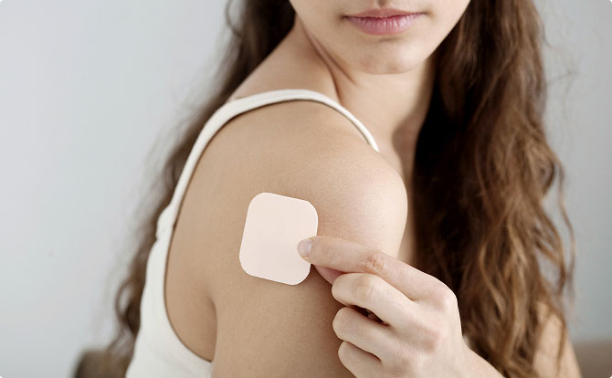 Uma mulher a aplicar um adesivo contracetivo na parte superior do braço.