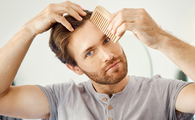 Um homem sem camisa a sorrir para o espelho enquanto passa a mão pelo cabelo