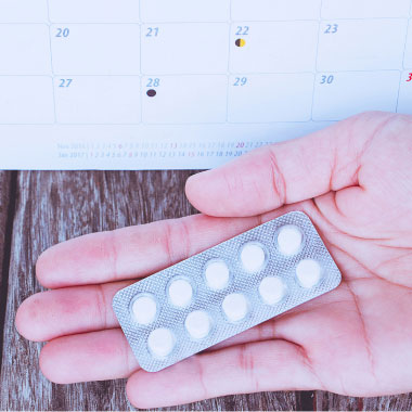 Alguém com um comprimido branco numa mão e um copo de água na outra.