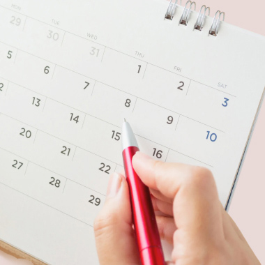 Närbild på en hand som håller en penna och pekar på ett datum i en kalender