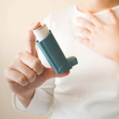 En ung kvinna sträcker sig efter en inhalator på bordet.