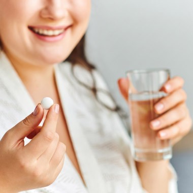 En kvinna som tar en vit tablett med ett glas vatten i andra handen