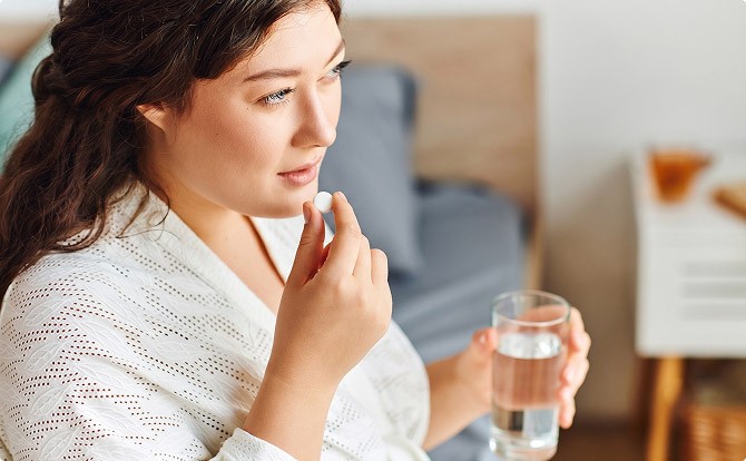 En ung kraftig kvinna tar en tablett med ett glas vatten